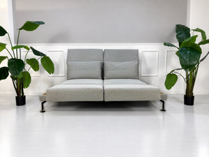 Gebrauchtes graues Brühl Moule Medium Designer Stoff Sofa mit Ablage und Hocker vor einer Wand, stilvoll und modern eingerichtet.