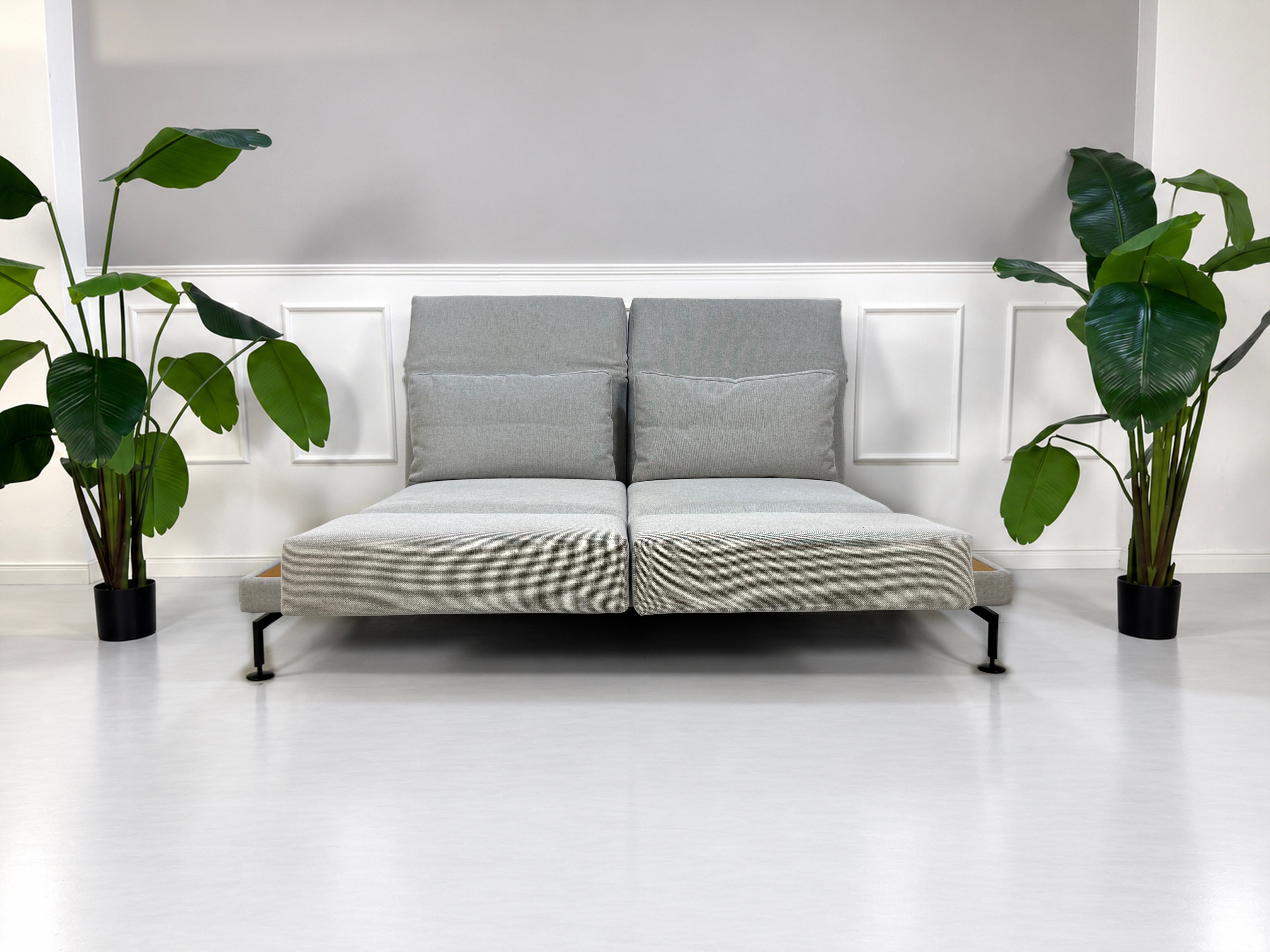 Gebrauchtes graues Brühl Moule Medium Designer Stoff Sofa mit Ablage und Hocker vor einer Wand, stilvoll und modern eingerichtet.