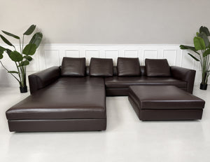 Gebrauchtes braunes Minotti Kline Designer Leder Ecksofa mit Hocker vor einer Wand, stilvoll und modern eingerichtet.