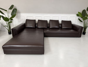 Gebrauchtes braunes Minotti Kline Designer Leder Ecksofa mit Hocker vor einer Wand, stilvoll und modern eingerichtet.