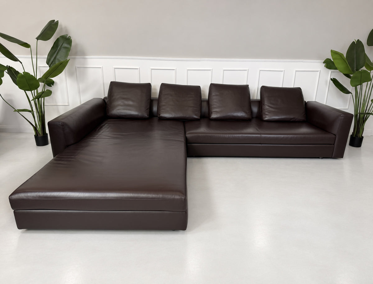 Gebrauchtes braunes Minotti Kline Designer Leder Ecksofa mit Hocker vor einer Wand, stilvoll und modern eingerichtet.
