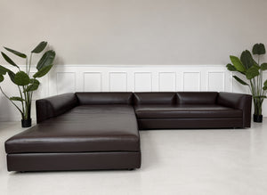 Gebrauchtes braunes Minotti Kline Designer Leder Ecksofa mit Hocker vor einer Wand, stilvoll und modern eingerichtet.