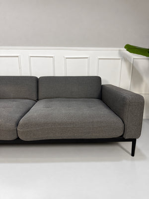 Gebrauchtes graues Rolf Benz Tira Designer Stoff Sofa vor einer Wand, stilvoll und modern eingerichtet.