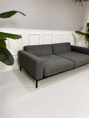 Gebrauchtes graues Rolf Benz Tira Designer Stoff Sofa vor einer Wand, stilvoll und modern eingerichtet.