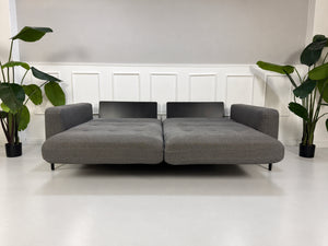 Gebrauchtes graues Rolf Benz Tira Designer Stoff Sofa vor einer Wand, stilvoll und modern eingerichtet.