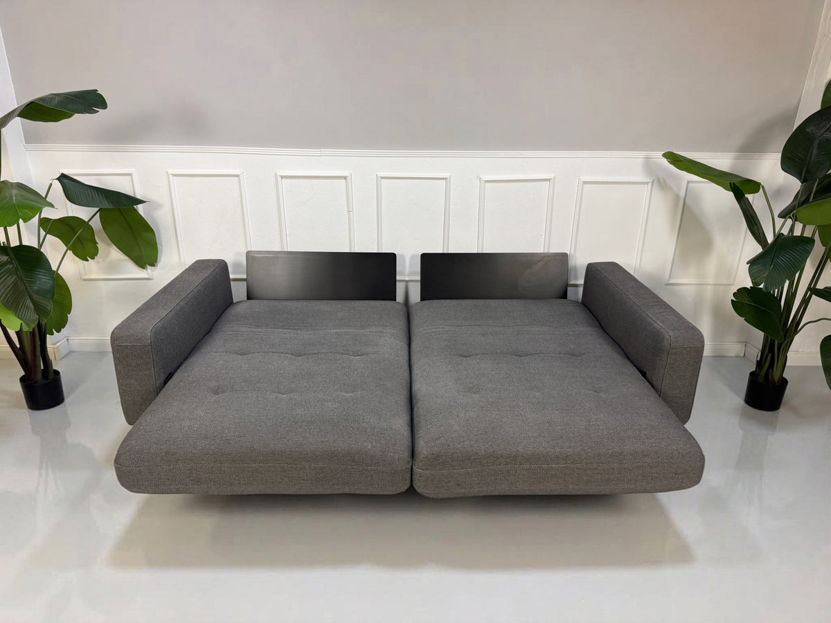 Gebrauchtes graues Rolf Benz Tira Designer Stoff Sofa vor einer Wand, stilvoll und modern eingerichtet.