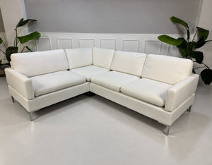 Gebrauchtes weißes Brühl Alba Designer Stoff Ecksofa vor einer Wand, stilvoll und modern eingerichtet.