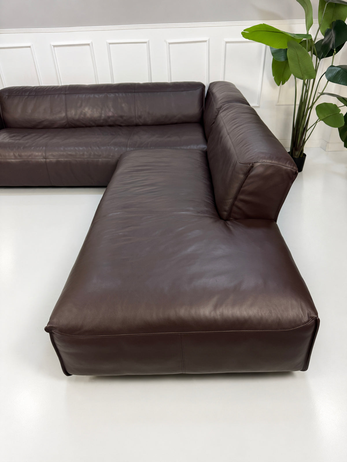 Gebrauchtes braunes Rolf Benz Mio Designer Leder Ecksofa vor einer Wand, stilvoll und modern eingerichtet.