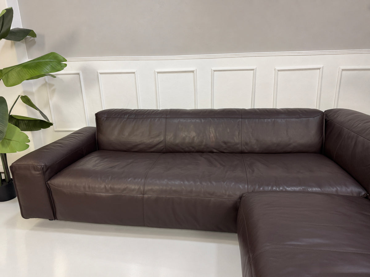 Gebrauchtes braunes Rolf Benz Mio Designer Leder Ecksofa vor einer Wand, stilvoll und modern eingerichtet.
