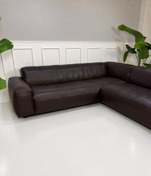 Gebrauchtes braunes Rolf Benz Mio Designer Leder Ecksofa vor einer Wand, stilvoll und modern eingerichtet.