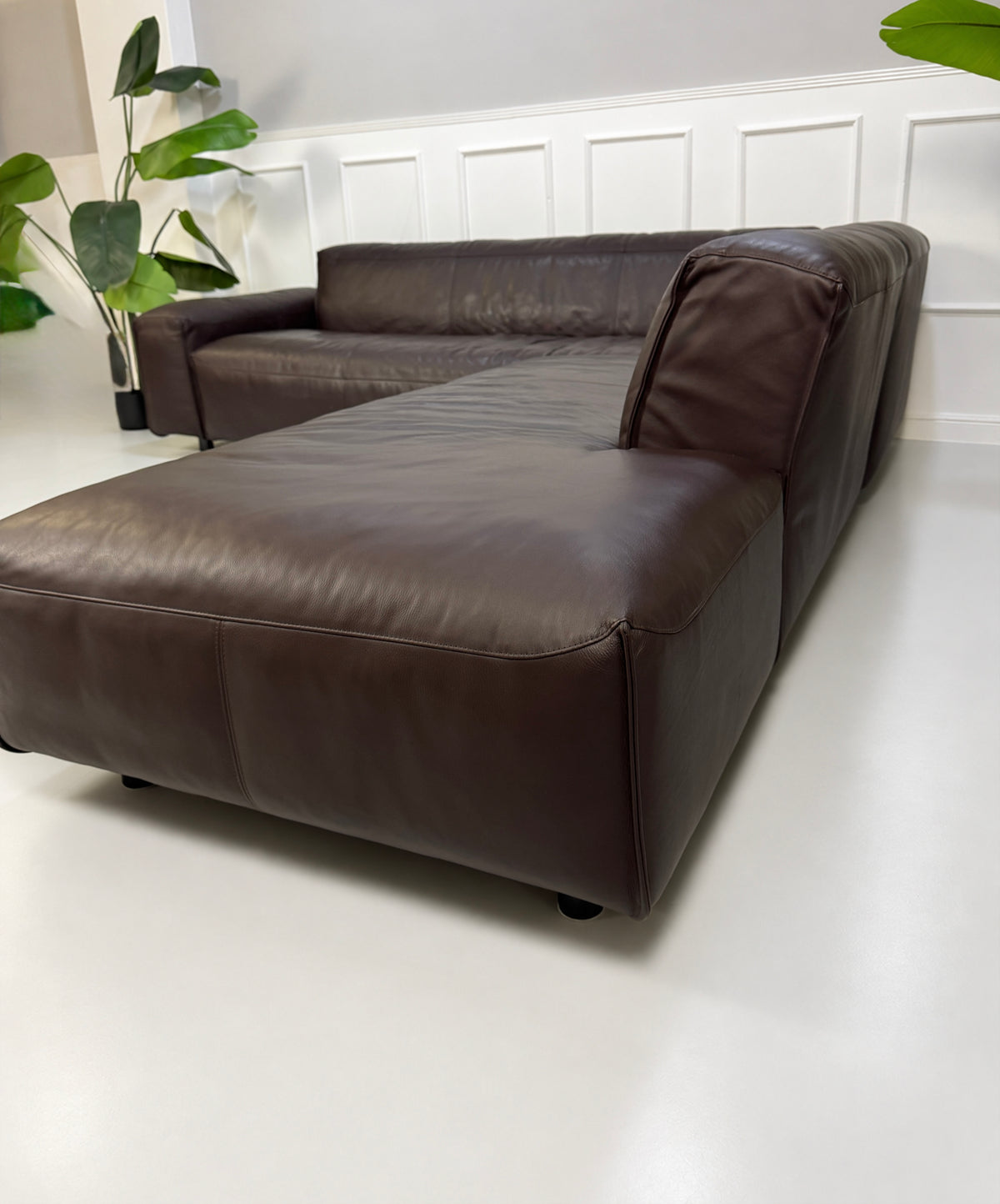 Gebrauchtes braunes Rolf Benz Mio Designer Leder Ecksofa vor einer Wand, stilvoll und modern eingerichtet.