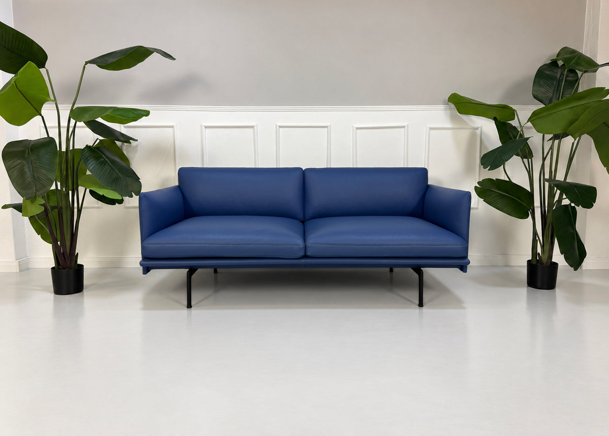 Gebrauchtes blaues Muuto Outline Designer Leder Sofa vor einer Wand, stilvoll und modern eingerichtet.