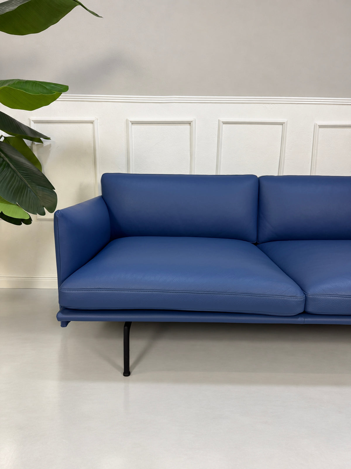 Gebrauchtes blaues Muuto Outline Designer Leder Sofa vor einer Wand, stilvoll und modern eingerichtet.