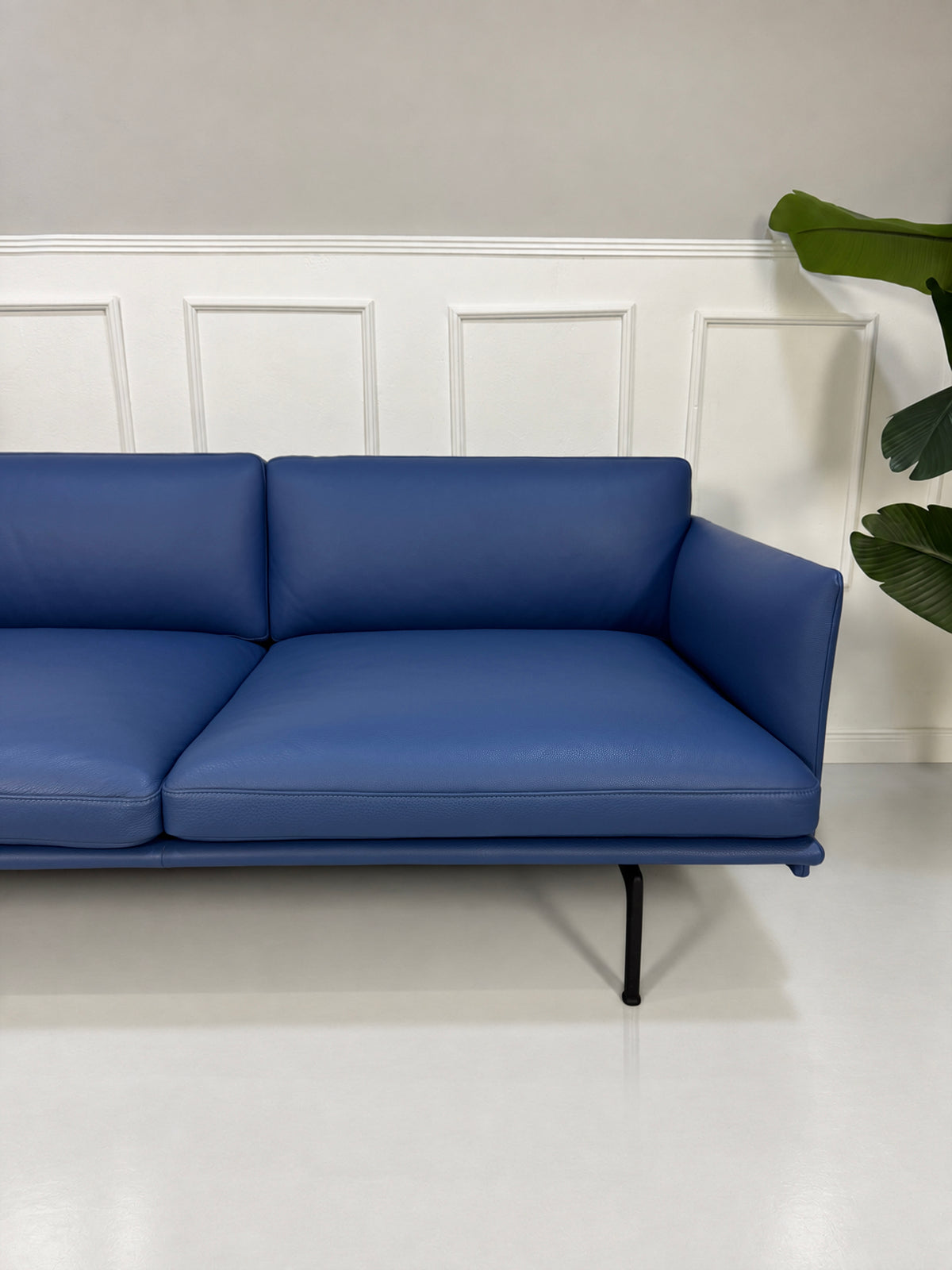 Gebrauchtes blaues Muuto Outline Designer Leder Sofa vor einer Wand, stilvoll und modern eingerichtet.