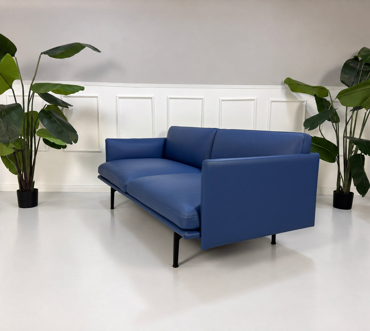 Gebrauchtes blaues Muuto Outline Designer Leder Sofa vor einer Wand, stilvoll und modern eingerichtet.