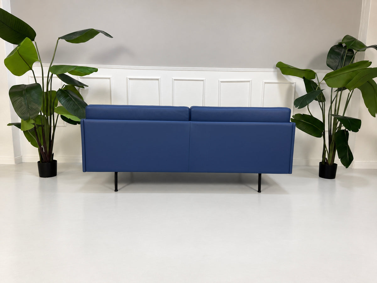 Gebrauchtes blaues Muuto Outline Designer Leder Sofa vor einer Wand, stilvoll und modern eingerichtet.