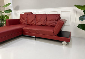 Gebrauchtes rotes Brühl Fourtwo Designer Leder Ecksofa vor einer Wand, stilvoll und modern eingerichtet.