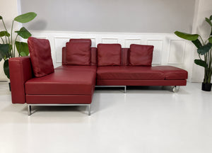 Gebrauchtes rotes Brühl Fourtwo Designer Leder Ecksofa vor einer Wand, stilvoll und modern eingerichtet.