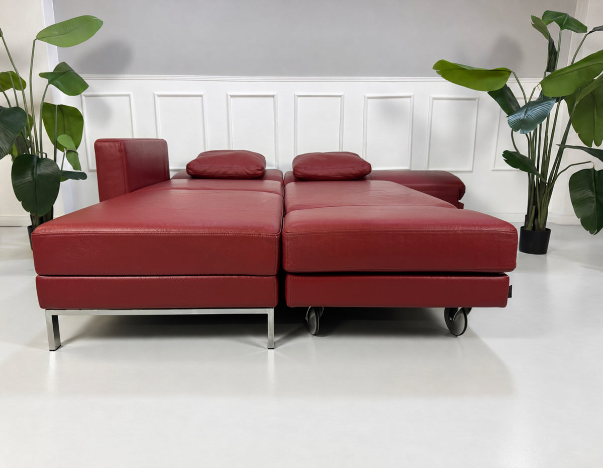 Gebrauchtes rotes Brühl Fourtwo Designer Leder Ecksofa vor einer Wand, stilvoll und modern eingerichtet.