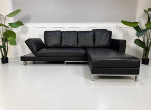 Gebrauchtes schwarzes Brühl Fourtwo Designer Leder Ecksofa vor einer Wand, stilvoll und modern eingerichtet.