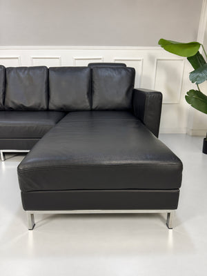 Gebrauchtes schwarzes Brühl Fourtwo Designer Leder Ecksofa vor einer Wand, stilvoll und modern eingerichtet.