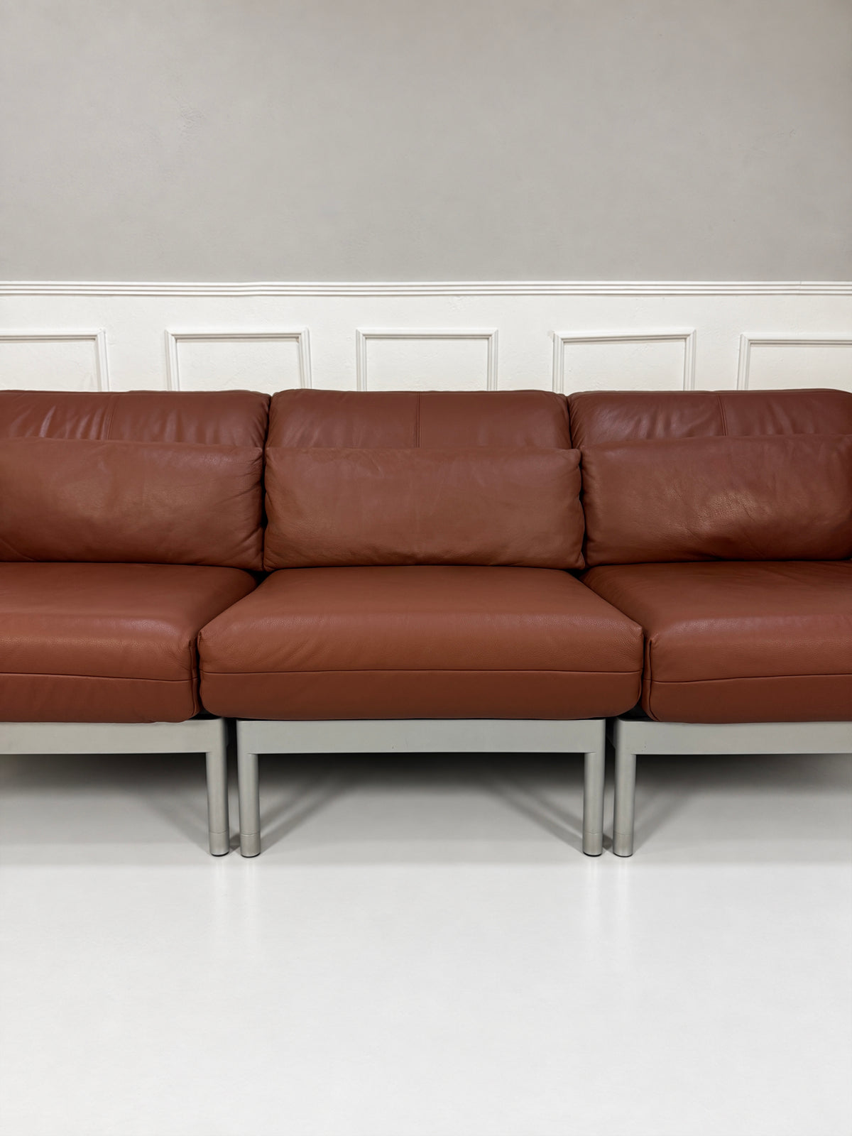 Gebrauchtes braunes Rolf Benz Plura 380 Designer Leder Sofa vor einer Wand, stilvoll und modern eingerichtet.