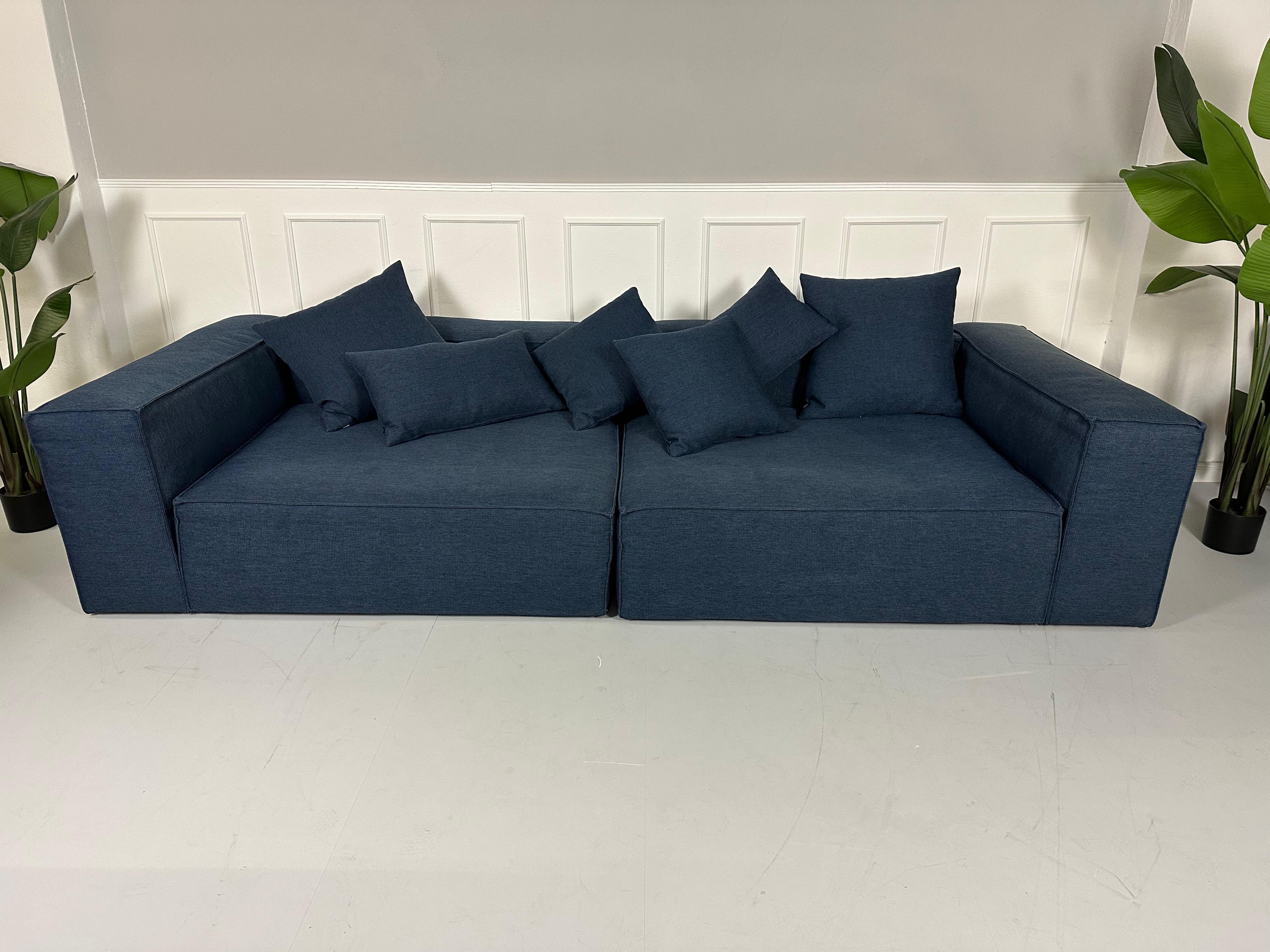 Gebrauchtes blaues Bolia Cosima Designer Stoff Sofa mit einem Hocker vor einer Wand, stilvoll und modern eingerichtet.