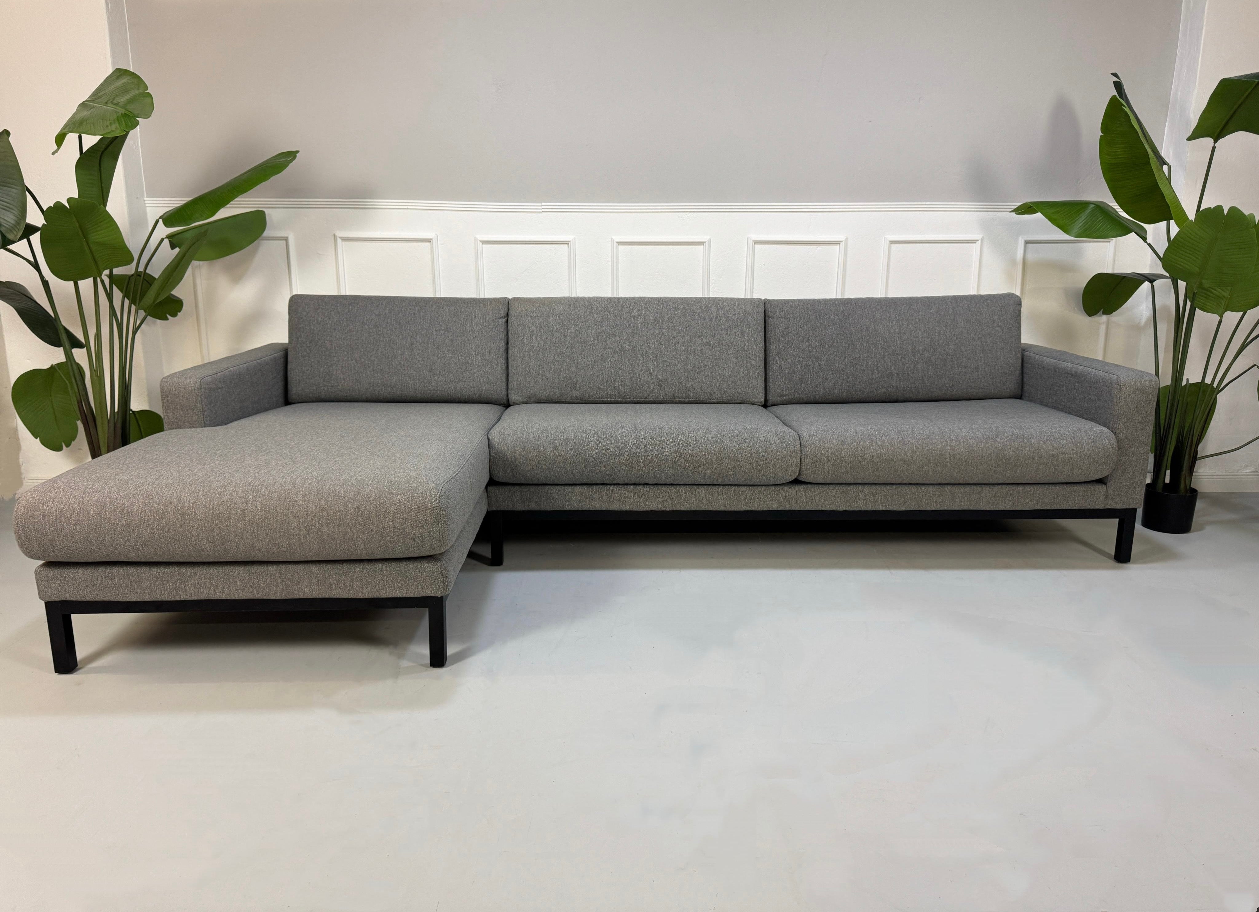 Gebrauchtes graues Bolia North Designer Stoff Sofa vor einer Wand, stilvoll und modern eingerichtet.