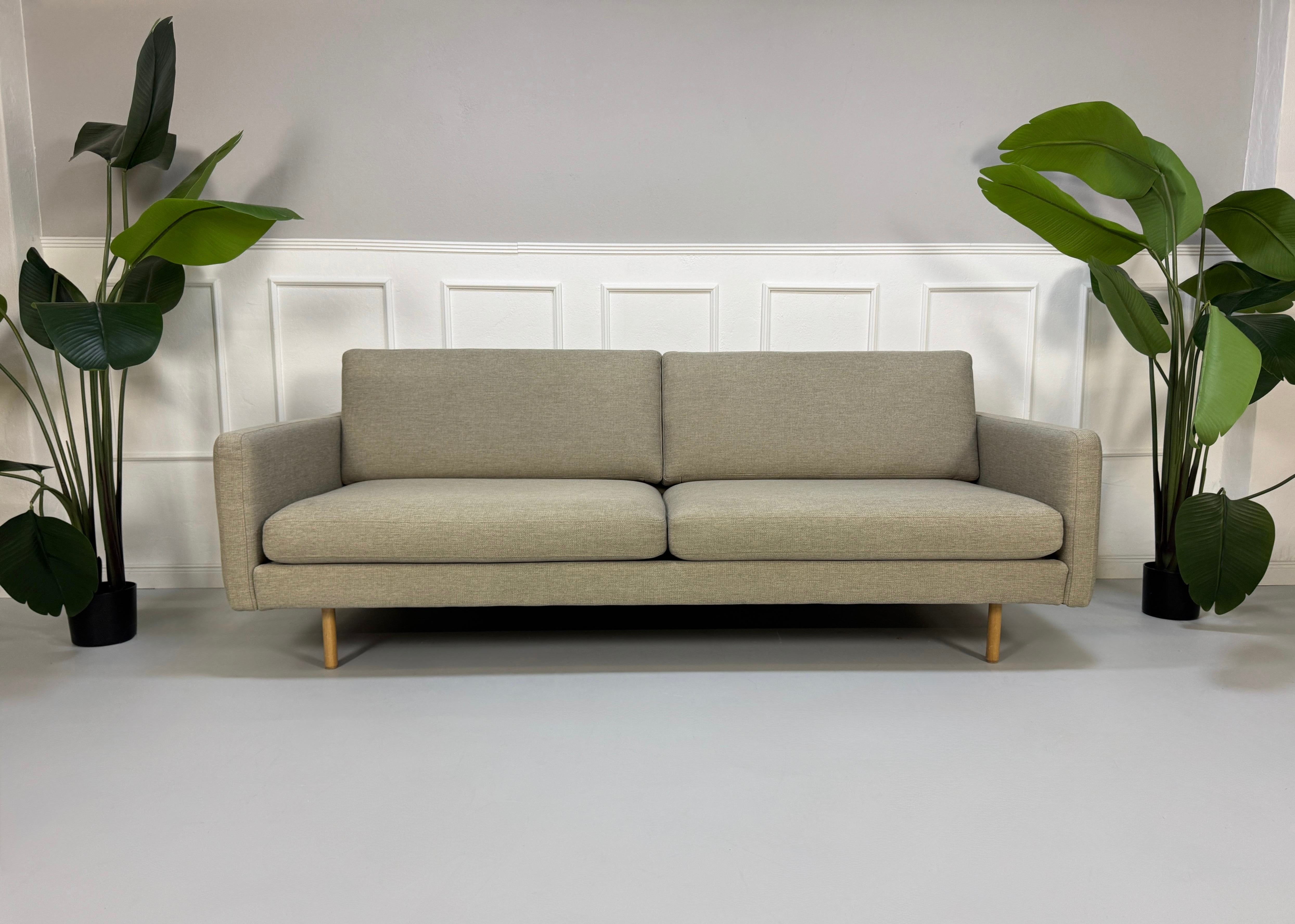 Gebrauchtes graues Bolia Remix Designer Stoff Sofa vor einer Wand, stilvoll und modern eingerichtet.