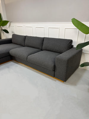 Gebrauchtes graues Bolia Sepia Designer Stoff Sofa vor einer Wand, stilvoll und modern eingerichtet.