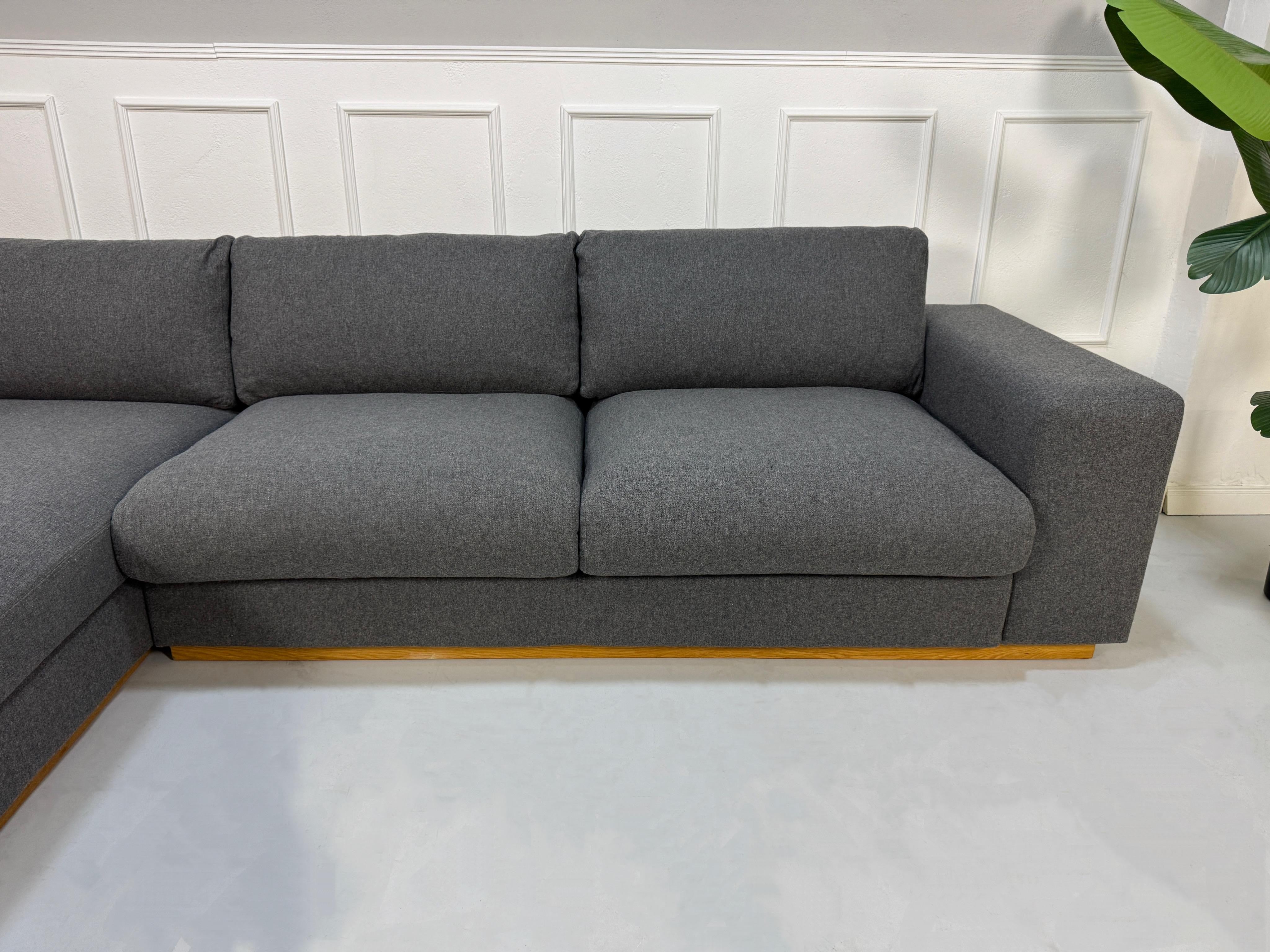 Gebrauchtes graues Bolia Sepia Designer Stoff Sofa vor einer Wand, stilvoll und modern eingerichtet.