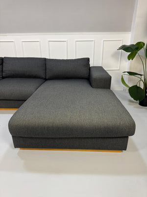 Gebrauchtes graues Bolia Sepia Designer Stoff Sofa mit Hocker vor einer Wand, stilvoll und modern eingerichtet.