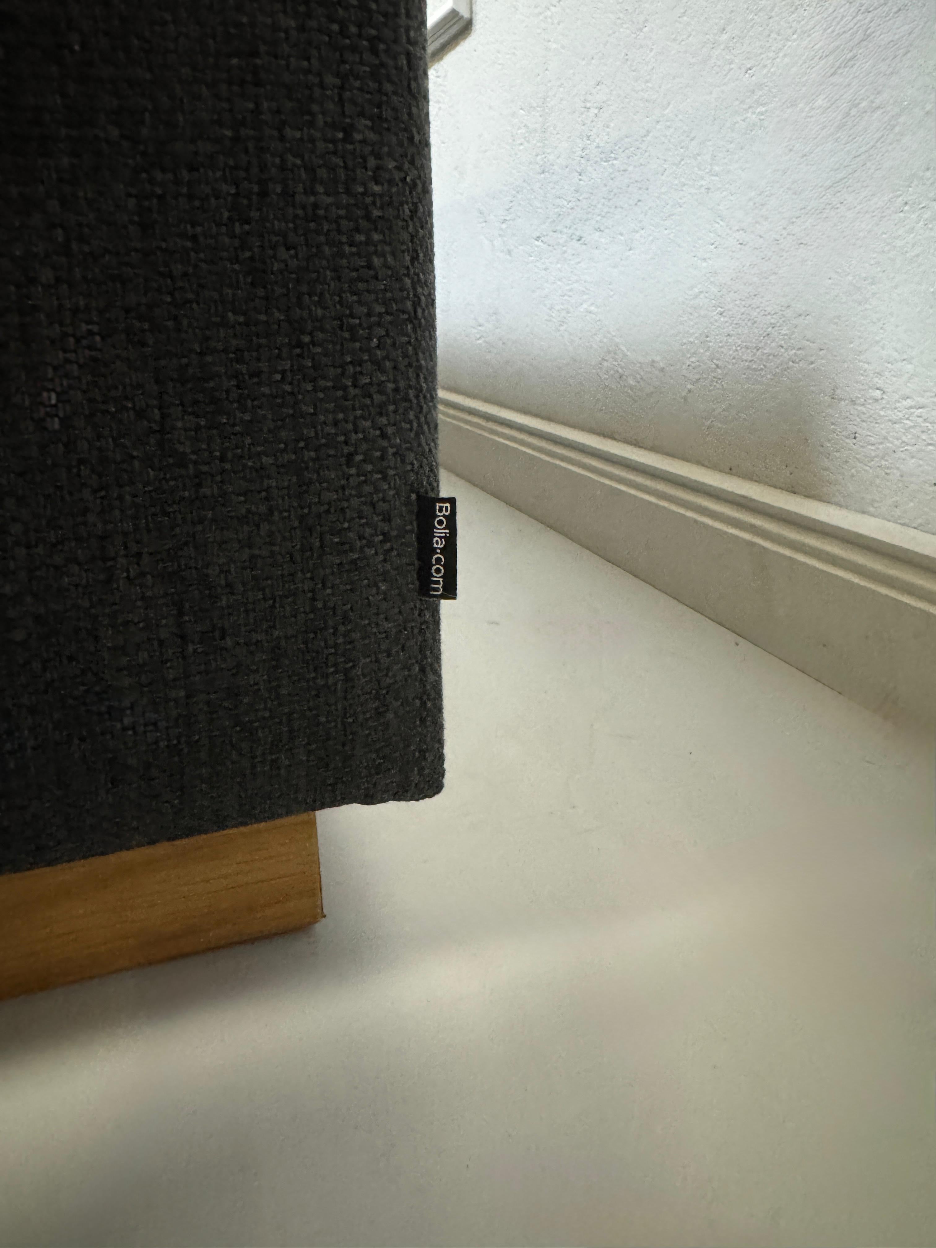 Gebrauchtes graues Bolia Sepia Designer Stoff Sofa mit Hocker vor einer Wand, stilvoll und modern eingerichtet.