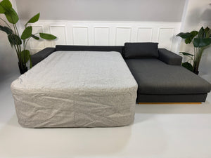 Gebrauchtes graues Bolia Sepia Designer Stoff Sofa mit Hocker vor einer Wand, stilvoll und modern eingerichtet.