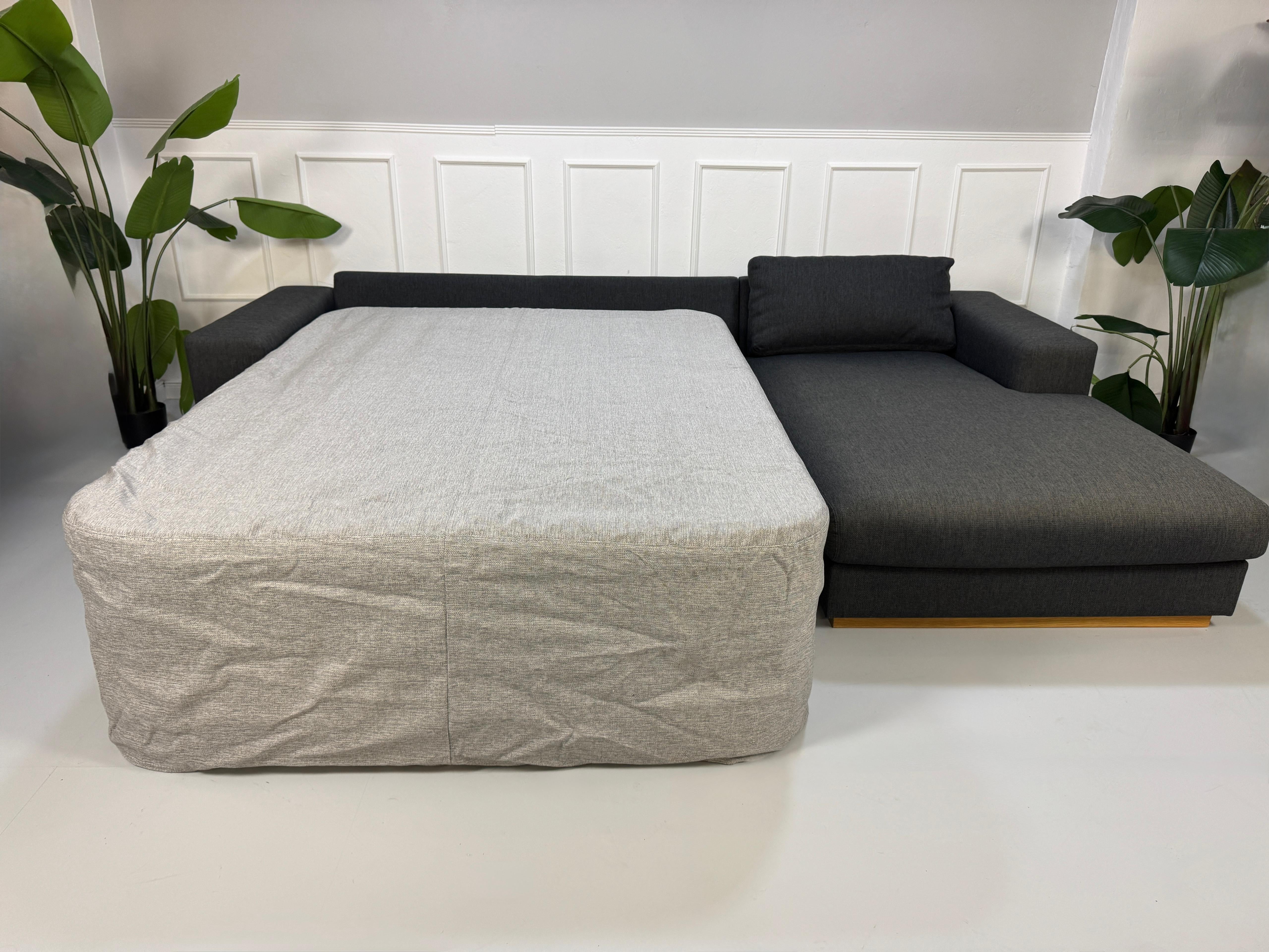 Gebrauchtes graues Bolia Sepia Designer Stoff Sofa mit Hocker vor einer Wand, stilvoll und modern eingerichtet.
