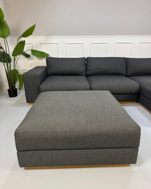 Gebrauchtes graues Bolia Sepia Designer Stoff Sofa mit Hocker vor einer Wand, stilvoll und modern eingerichtet.