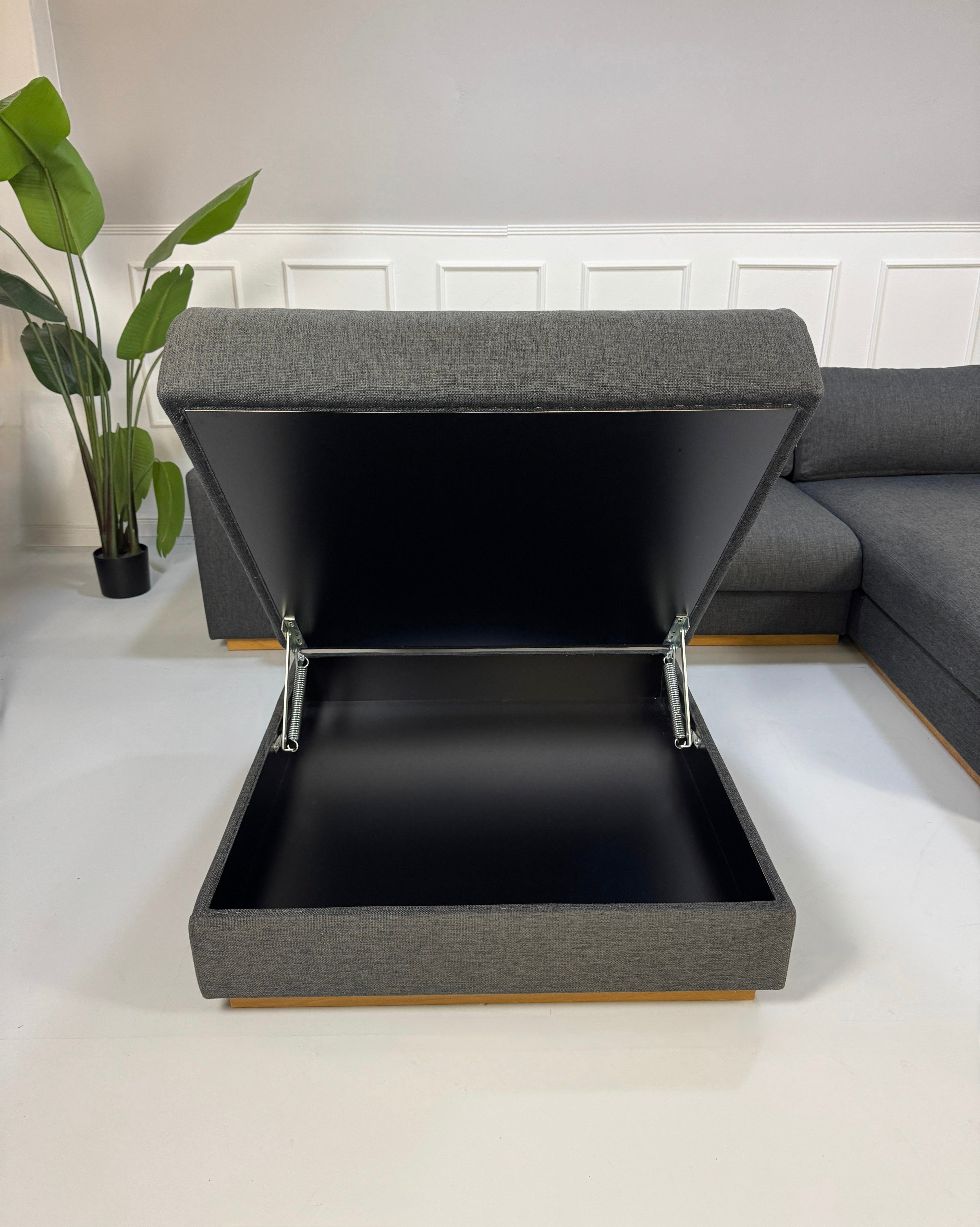 Gebrauchtes graues Bolia Sepia Designer Stoff Sofa mit Hocker vor einer Wand, stilvoll und modern eingerichtet.