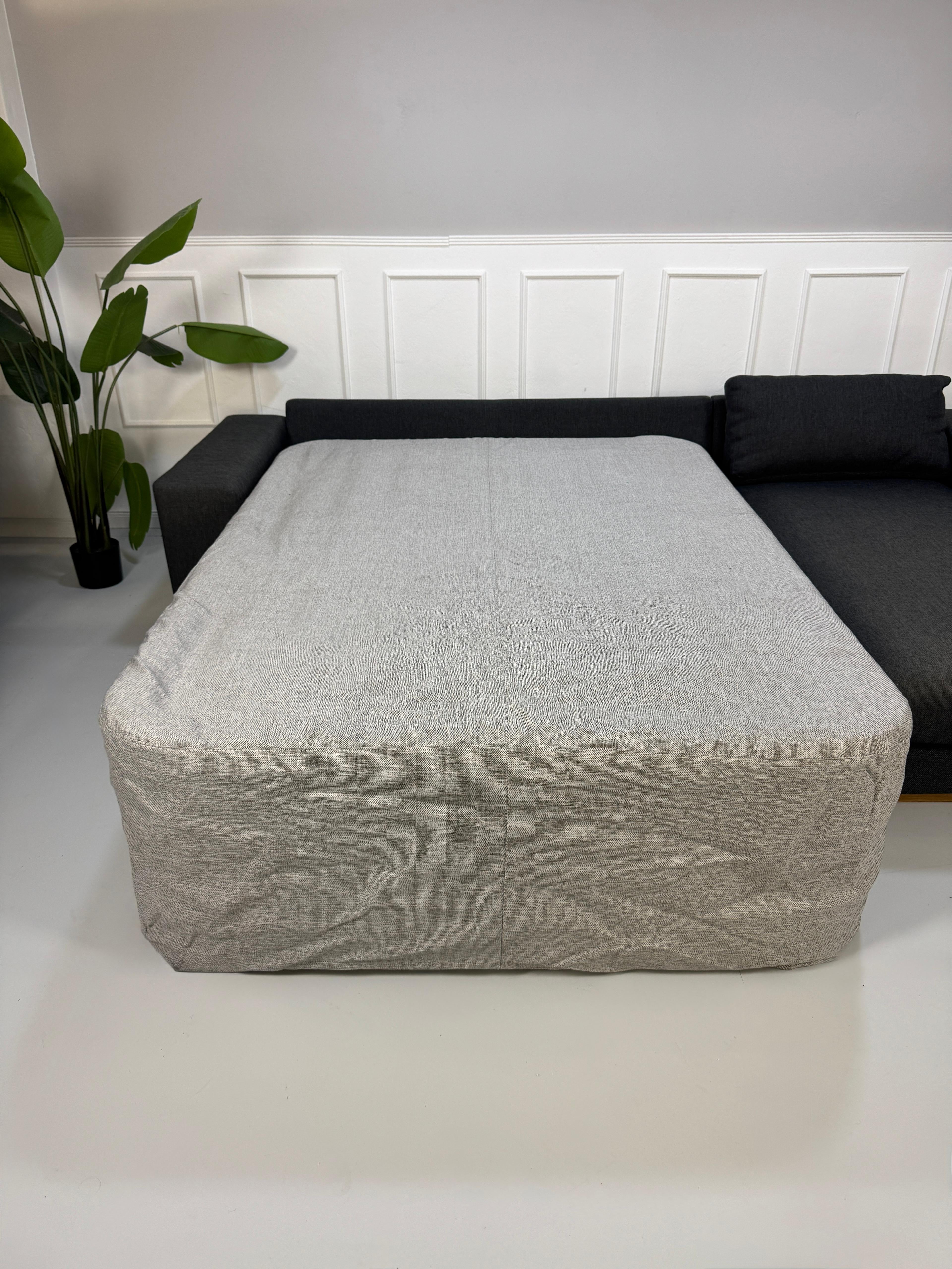 Gebrauchtes graues Bolia Sepia Designer Stoff Sofa mit Hocker vor einer Wand, stilvoll und modern eingerichtet.