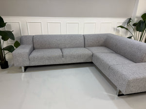 Gebrauchtes graues Bolia Seville Designer Stoff Ecksofa vor einer Wand, stilvoll und modern eingerichtet.