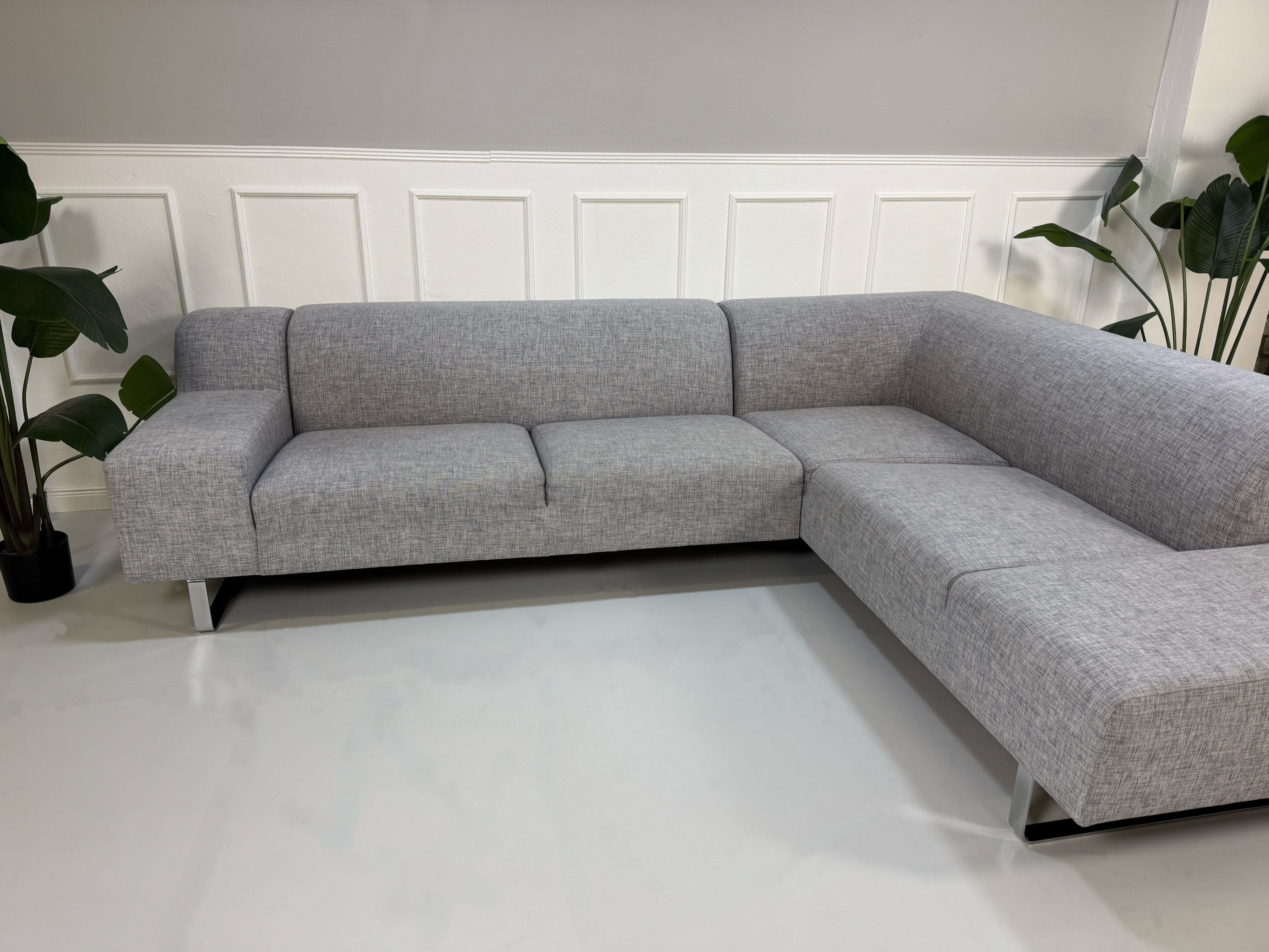 Gebrauchtes graues Bolia Seville Designer Stoff Ecksofa vor einer Wand, stilvoll und modern eingerichtet.