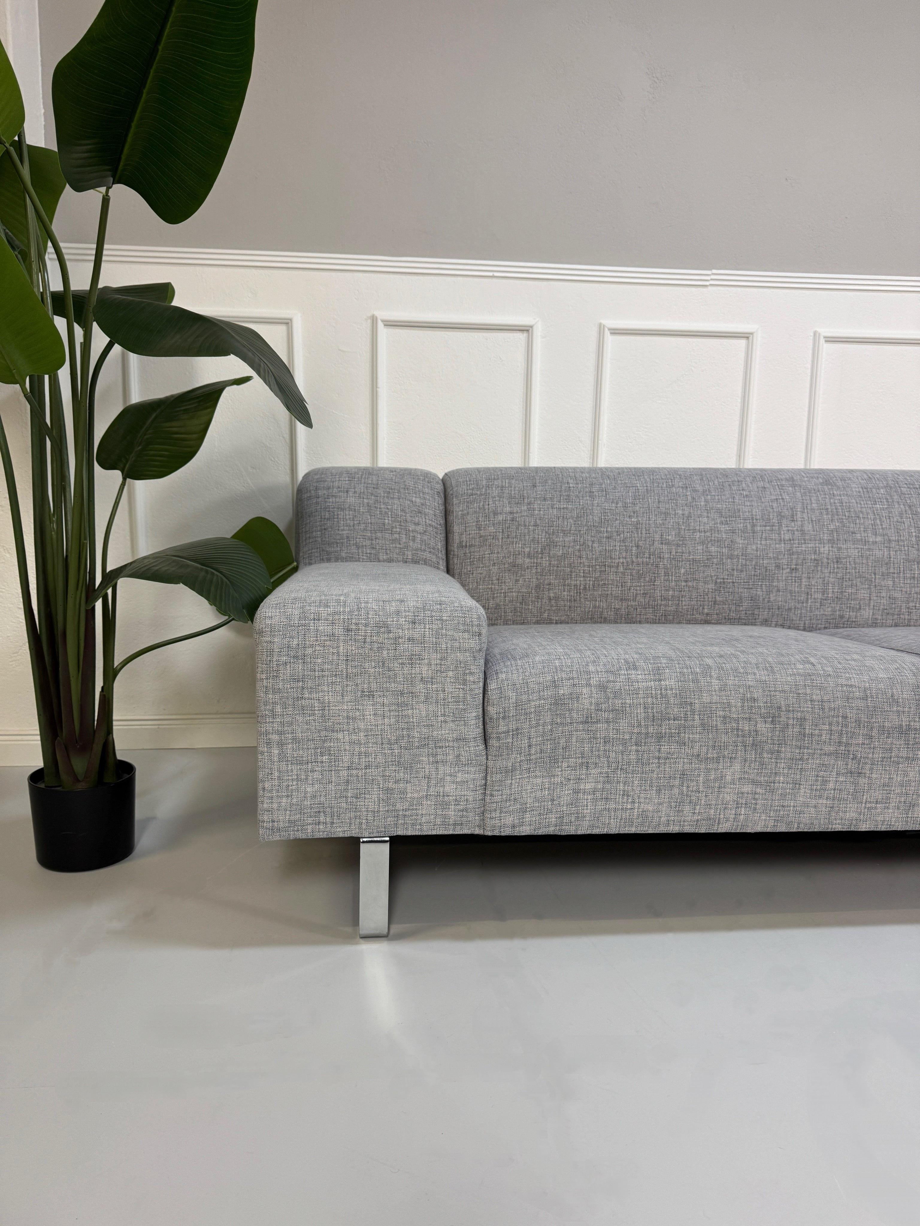 Gebrauchtes graues Bolia Seville Designer Stoff Ecksofa vor einer Wand, stilvoll und modern eingerichtet.