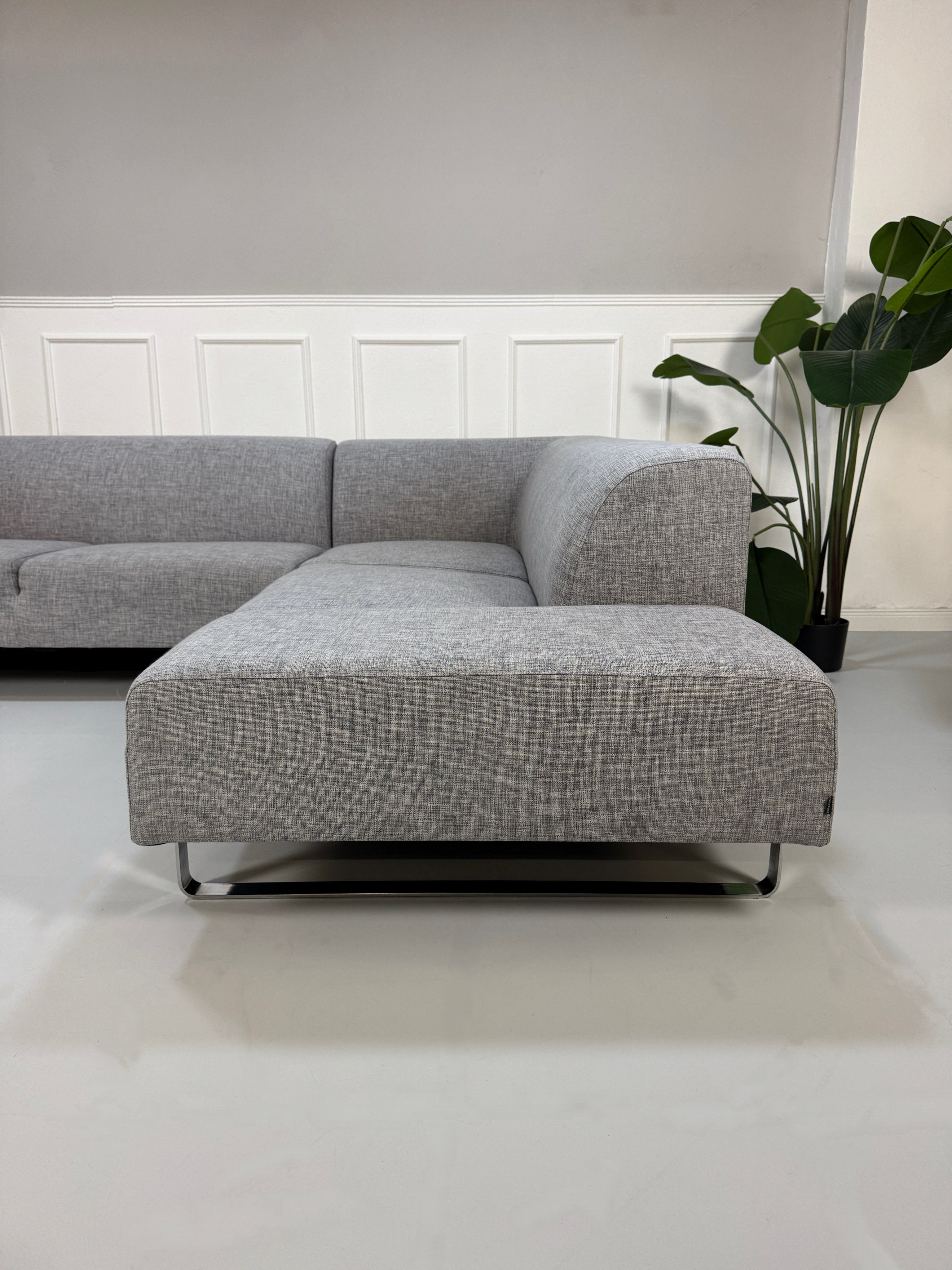 Gebrauchtes graues Bolia Seville Designer Stoff Ecksofa vor einer Wand, stilvoll und modern eingerichtet.