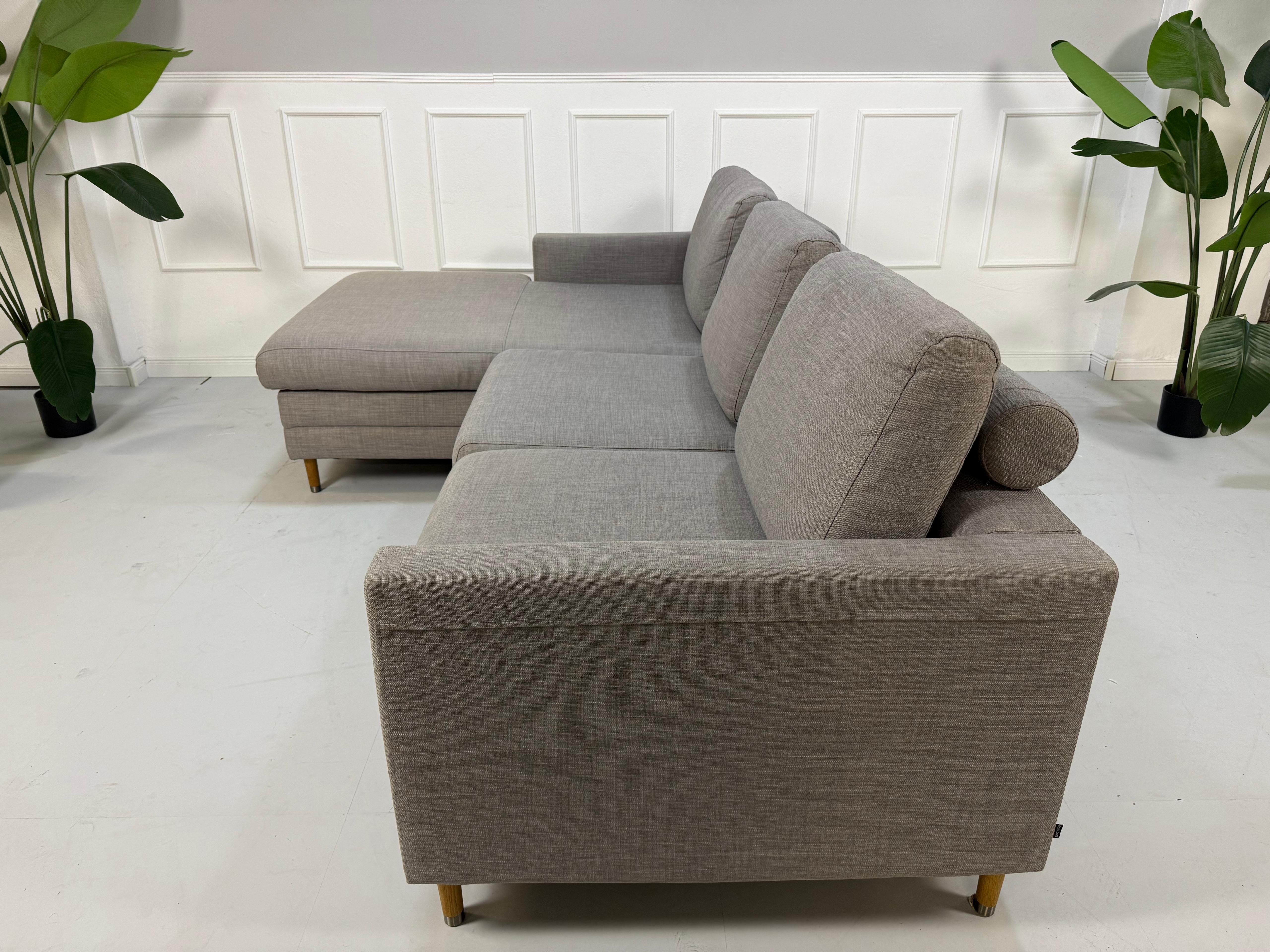 Gebrauchtes graues Bolia Designer Stoff Sofa vor einer Wand, stilvoll und modern eingerichtet.