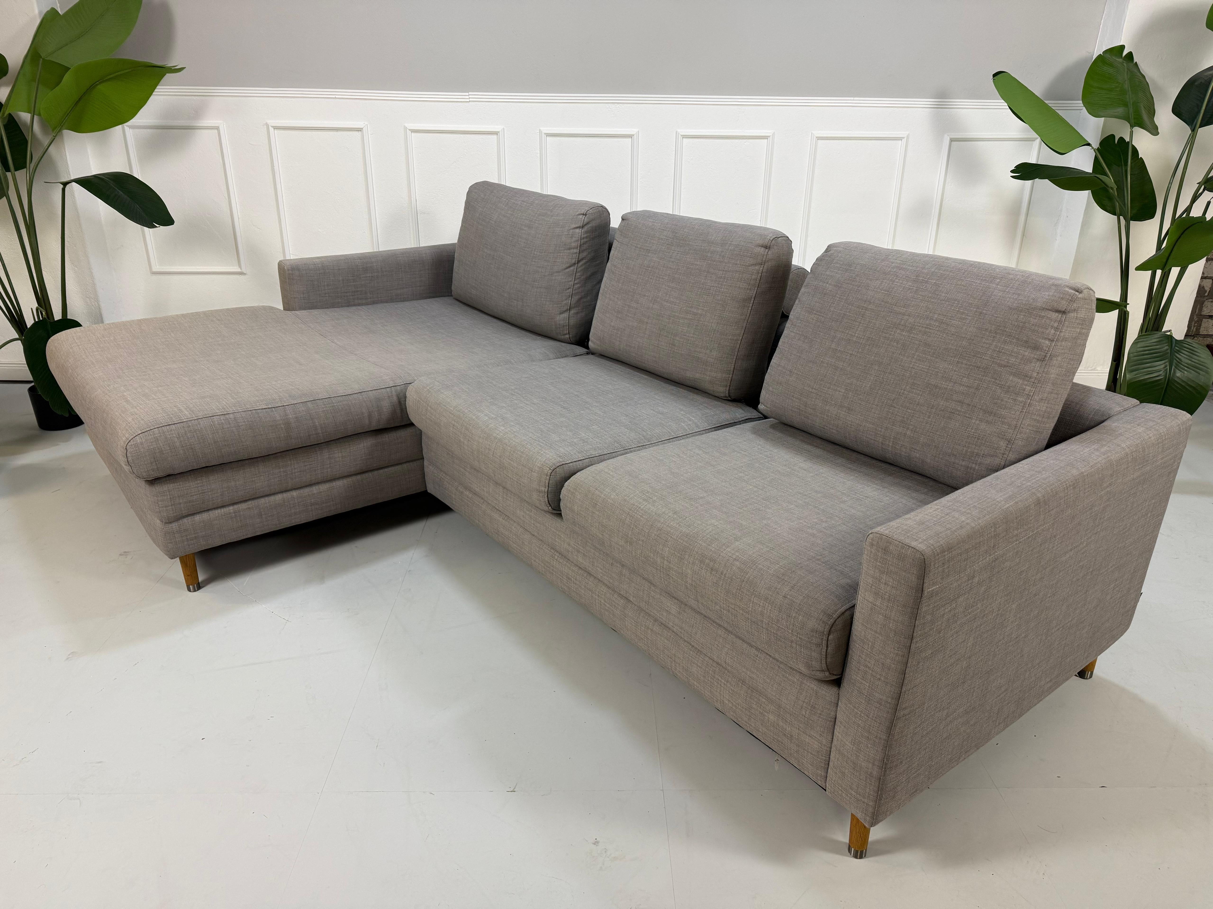 Gebrauchtes graues Bolia Designer Stoff Sofa vor einer Wand, stilvoll und modern eingerichtet.