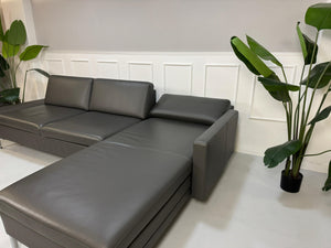 Gebrauchtes graues Brühl Alba Designer Leder Sofa vor einer Wand, stilvoll und modern eingerichtet.