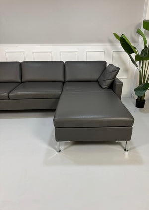 Gebrauchtes graues Brühl Alba Designer Leder Sofa vor einer Wand, stilvoll und modern eingerichtet.