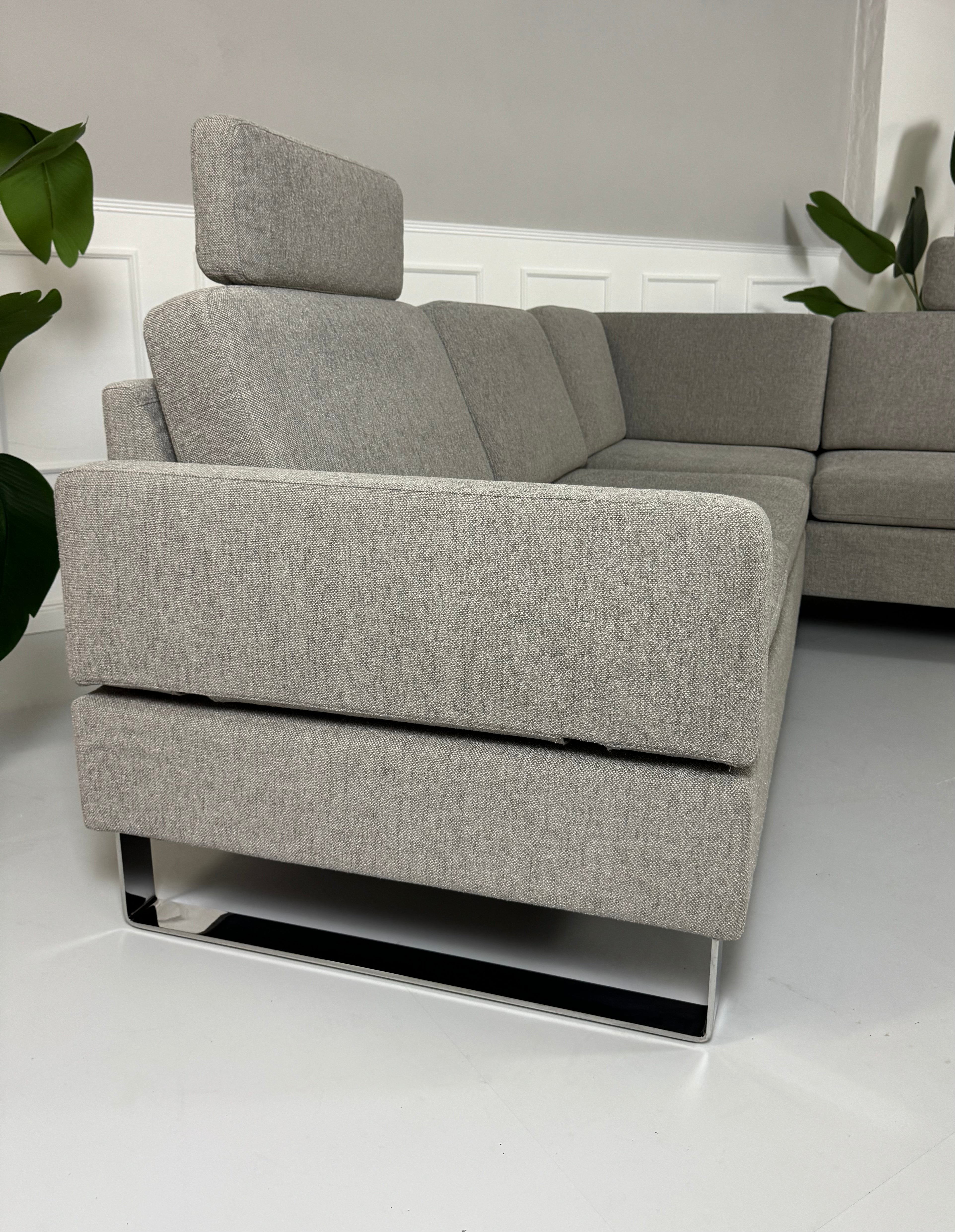 Gebrauchtes graues Brühl Alba Stoff Ecksofa vor einer Wand, stilvoll und modern eingerichtet.