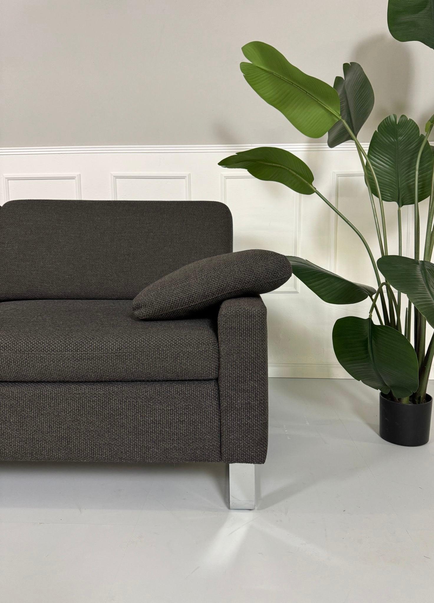 Gebrauchtes grau braunes Brühl Alba Stoff Sofa vor einer Wand, stilvoll und modern eingerichtet.