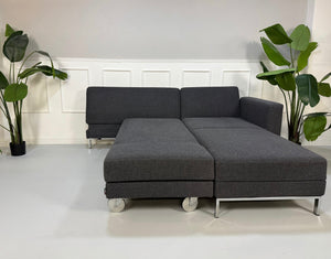 Ausstellungsstück Brühl Fourtwo Grau  Designer Stoff Sofa vor einer Wand, stilvoll und modern eingerichtet.
