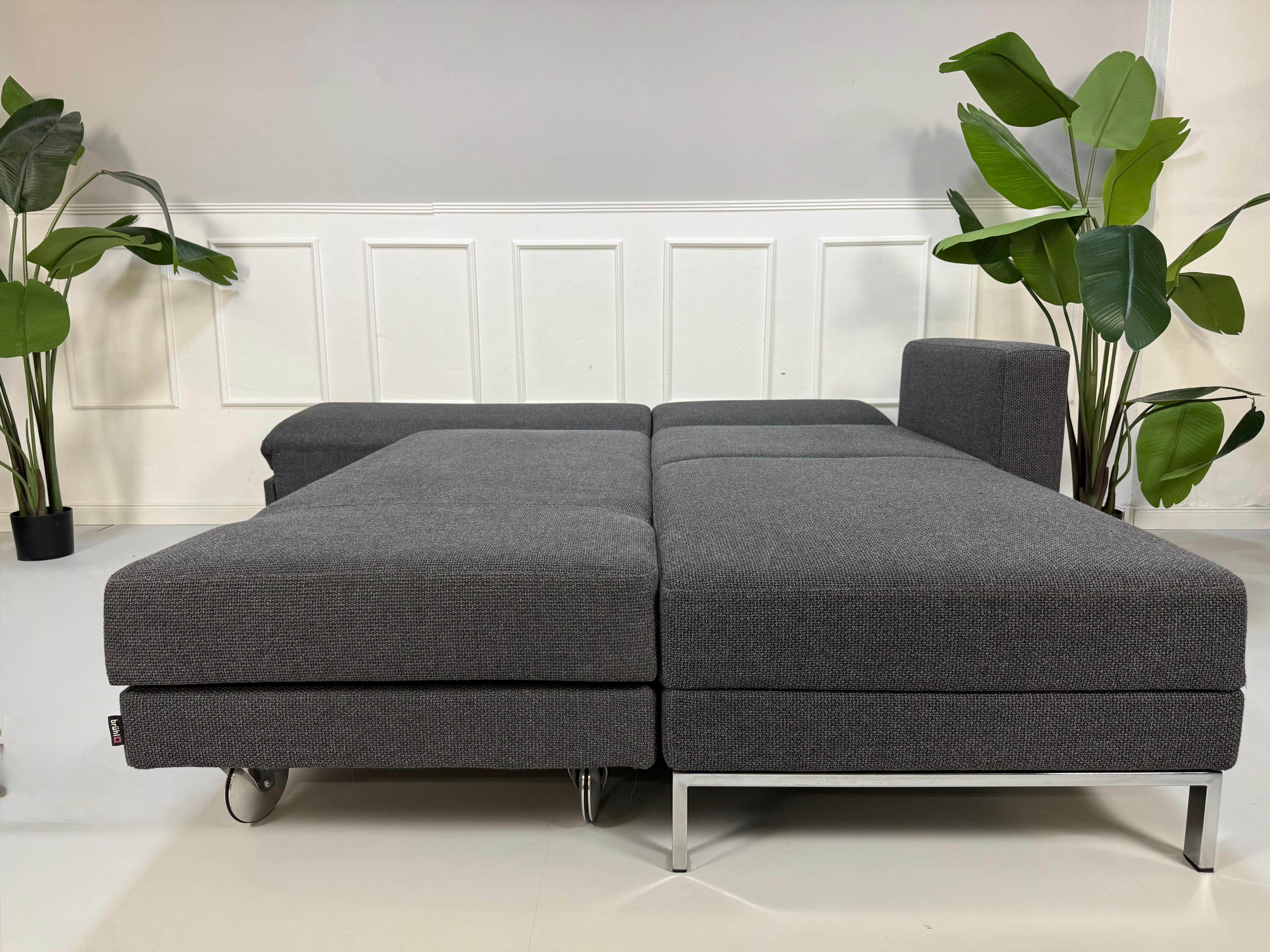 Ausstellungsstück Brühl Fourtwo Grau  Designer Stoff Sofa vor einer Wand, stilvoll und modern eingerichtet.